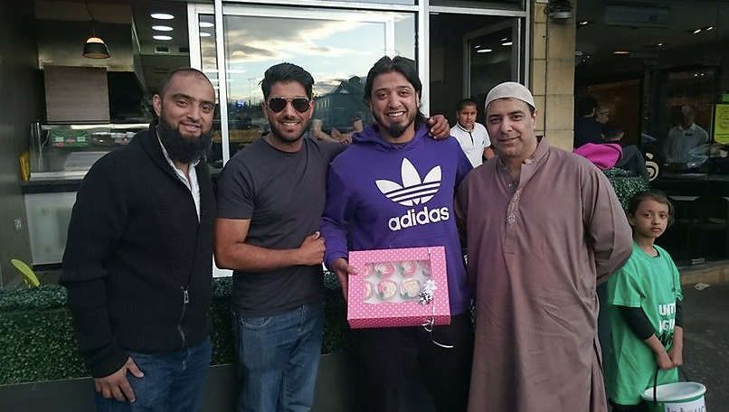Four men pose in a line holding a box of cupcakes.